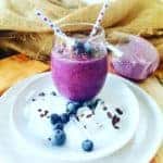 Blueberry Smoothie in a glass on a white plate with a blue straw