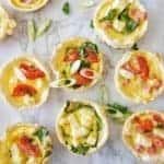 Mini Quiches on a white background garnished with sliced shallots