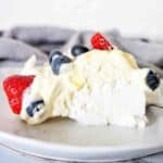 Slice of pavlova with fresh fruit on white plate.