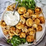 Breaded mushrooms on white plate with small bowl of sauce.