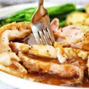 Roast pork on white plate with gravy and vegetables.