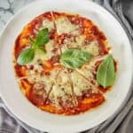 Air fryer tortilla pizza with pepperoni and cheese sliced on white plate.