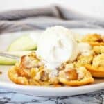 Apple pie tart with vanilla ice cream on white plate.