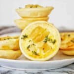 Custard tarts with apples pieces stacked on white plate.