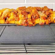 Cooked bacon cheese bread in loaf tin on wire rack.