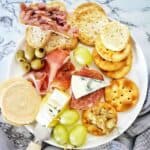 Cheese and crackers with cured meats on white plate.