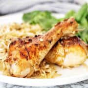 Cooked chicken legs on white plate with rice and greens.