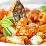 Fork being pushed into bowl of pasta with fresh basil leaves.