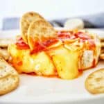Baked brie pepper jelly with crackers on white plate.