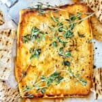 Baked feta on white plate with thyme and pita chips.