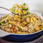 Spoon holding basmati fried rice over white baking dish of the same.
