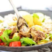 Fork being pushed into beef massaman in black bowl.