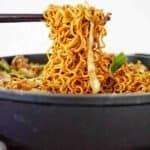 Chopsticks holding noodles above a black pan