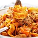 Fork being twirled in bowl of ragu with pappardelle.