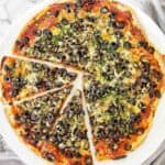 Pizza with black olives and capers on white plate.