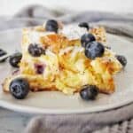 Slice of blueberry croissant bake on white plate with extra blueberries.