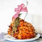 Glazed ham with bourbon and maple syrup on white plate with red ribbon.