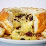 Cheese dripping out of brie bread bowl on white plate.