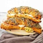 Two croissants with seeds on top stacked on white plate with grey napkin below.