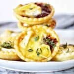 Brie and cranberry tarts on white plate with thyme leaves.
