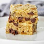 Two butter pecan blondies with chocolate chips stacked on a white plate.