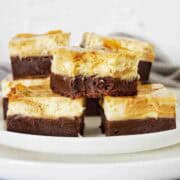 Brownies with a caramel cheesecake layer spread out on a white plate.