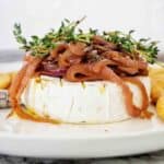 Baked brie wheel on white plate with caramelised onions and thyme.