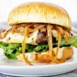 Burger with caramelized onions on white plate with lettuce and cheese.