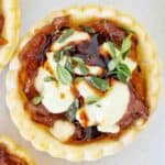 Goats cheese and caramelised onion tart with thyme on white plate.