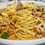 Fork being twirled in carbonara with mushrooms and bacon on white plate