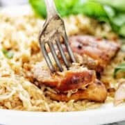 Fork being pushed into chicken on white plate with rice.