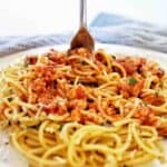 Fork being twirled in chicken spaghetti bolognese on white plate