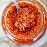 Chilli and tomato jam in clear glass with silver spoon.