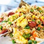 Spoon stirring chorizo rice on white plate.