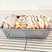 Dusted cinnamon sugar bread in loaf tin on wire rack.
