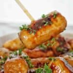 Skewer holding mini sausage over bowl of the same.