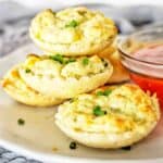 Mini crab tarts stacked on white plate with sauce.