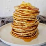 Crispy pancake stack on white plate with butter and maple syrup toppings