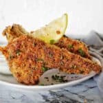 Crumbed lamb cutlets on white plate with lemon wedges and yogurt sauce.