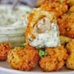 Bite out of crumbed mushroom that has been dipped in sauce on white plate.