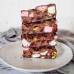 Pieces of chopped dark chocolate rocky road stacked on a white plate.