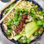 Dumplings with noodles in blue pattered bowl with chopsticks.