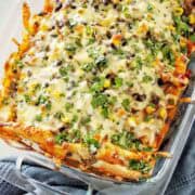 Cooked beef enchiladas in large casserole dish with cheese and chopped parsley on top.