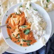 Butter Chicken in white bowl with rice , poppadoms, and coriander