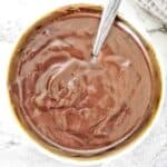 Chocolate icing in small bowl with silver spoon.