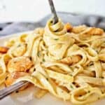 Fork being twirled in scallop pasta on white plate.