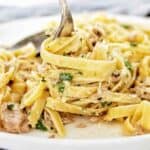 Fork being twirled in plate of fettuccine alfredo with tuna.