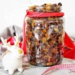 Fruit mince in clear jar with red ribbon and reindeer figurine on white background.