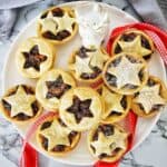 Baked fruit mince tarts on white plate with red ribbon and reindeer figurine.