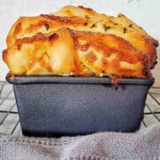 Cooked garlic and herb bread in loaf tin seen from the side.